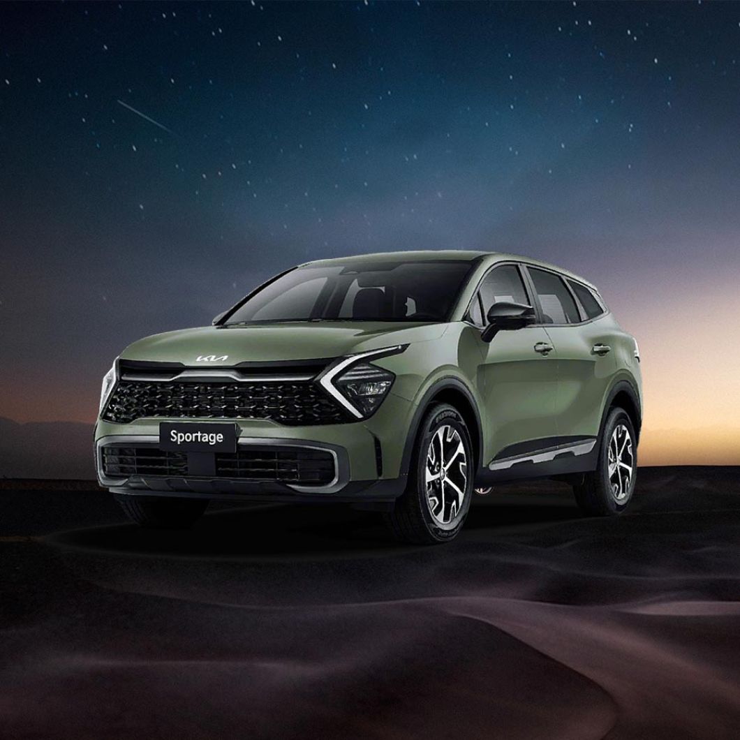 A green Kia Sportage SUV parked on a desert-like terrain under a starry night sky with a hint of sunset glow in the background.