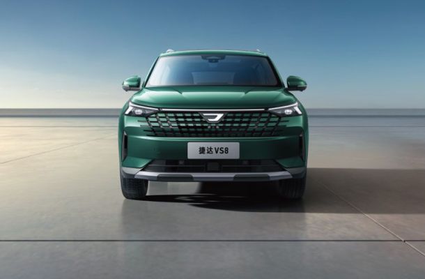 Front view of a teal Jetta VS8 SUV, featuring a bold grille and sleek headlights, parked on a smooth surface with a clear blue sky backdrop.