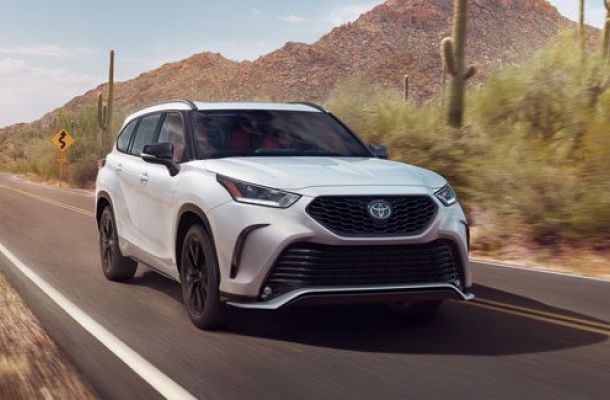 White Toyota SUV driving on desert road: cactus/mountain backdrop, bold grille, black alloy wheels.