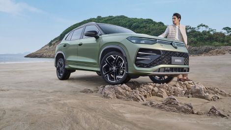 A green Volkswagen Tayron L SUV parked on a scenic mountain road at sunset.