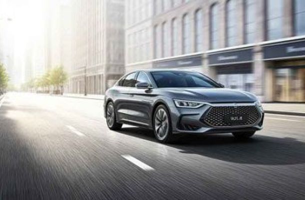 A sleek silver sedan driving on an urban street with buildings in the background.