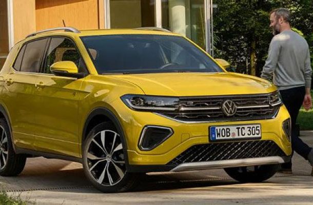 A bright 2025 Volkswagen T-Cross with license plate WOB TC 305, parked near a building as a man walks by, surrounded by greenery.