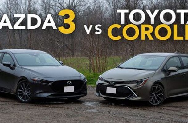 Side-by-side view of a dark gray Mazda3 (left) and a gray Toyota Corolla (right) on a gravel surface. Text "MAZDA3 vs TOYOTA COROLLA" (white/yellow) overlays, framing a car comparison.