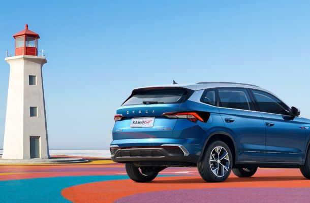 A blue Skoda Kamiq GT SUV parked on a colorful platform next to a lighthouse, with a clear blue sky in the background.