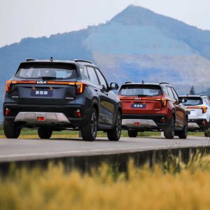 KIA Seltos 2023 1.5L CVT Premium Edition gallery Multiple Kia SUVs driving on a road with mountains in the background.