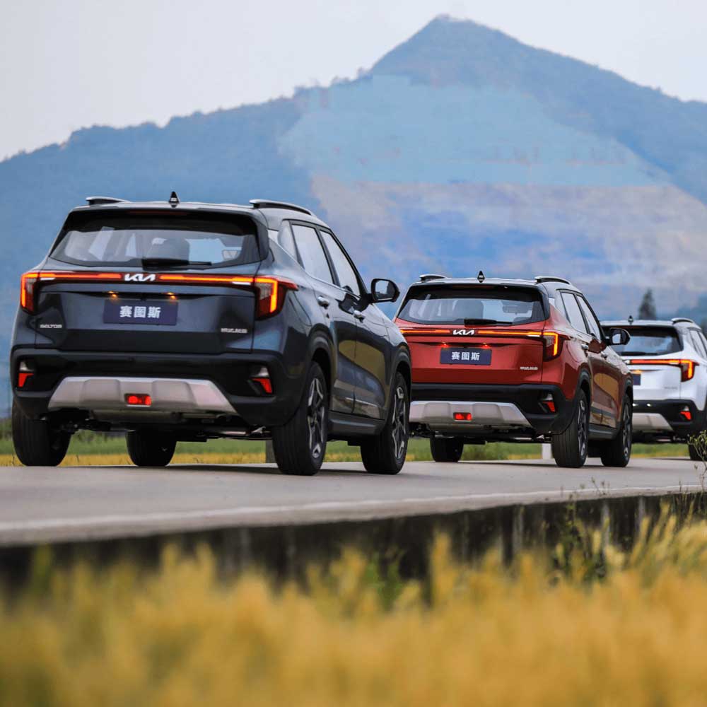 KIA Seltos 2023 1.5L CVT Premium Edition gallery Multiple Kia SUVs driving on a road with mountains in the background.