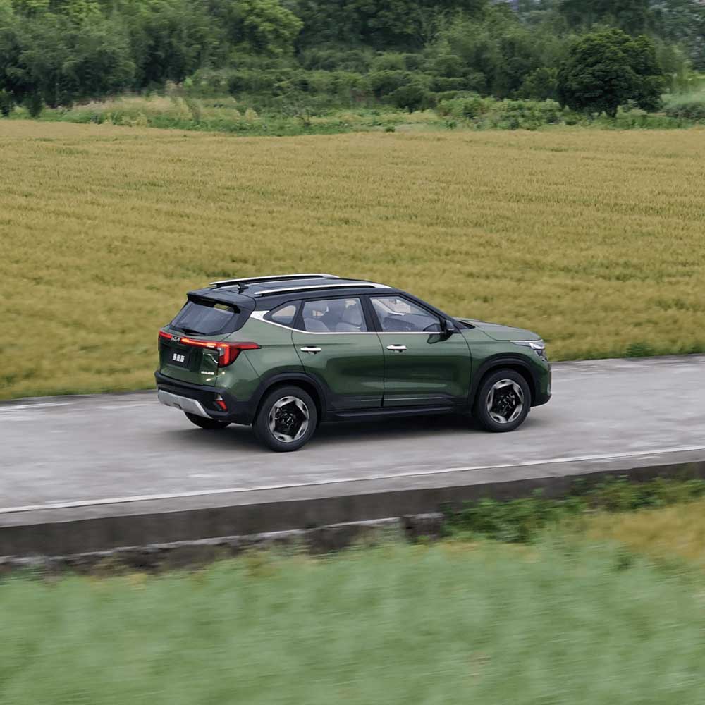 KIA Seltos 2023 1.5L CVT Premium Edition gallery3 A dark green SUV driving on a road next to a wheat field.