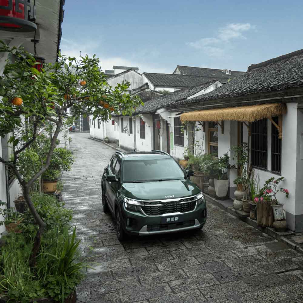 KIA Seltos 2023 1.5L CVT Premium Edition gallery5 A dark green Kia SUV parked in a narrow alley of an old town.