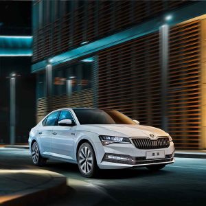 A white Škoda Superb sedan driving on a city street at night.