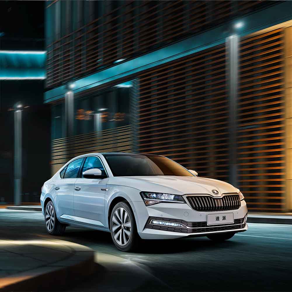 A white Škoda Superb sedan driving on a city street at night.