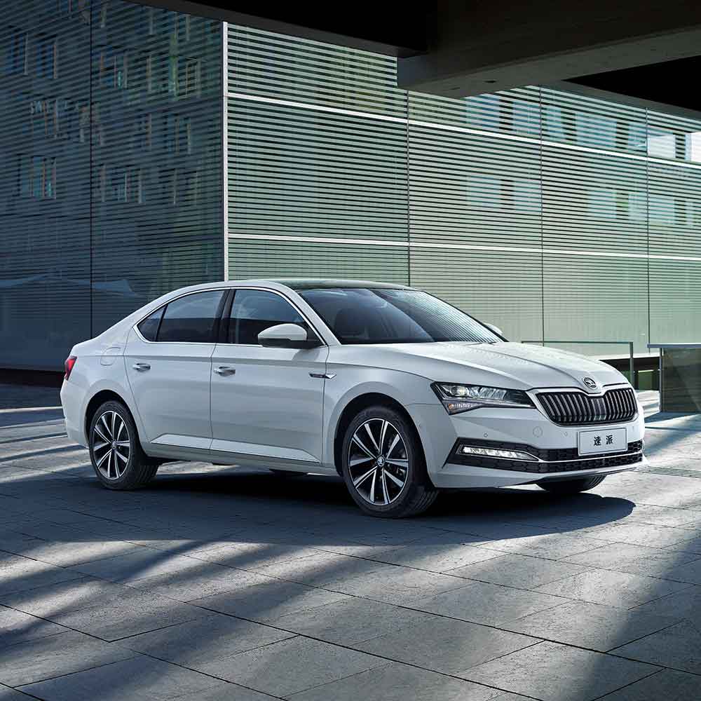 A white Škoda Superb sedan parked in front of a modern building.