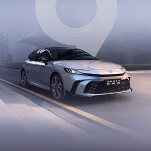 A silver Toyota Camry driving on the road with a large number "9" in the background.