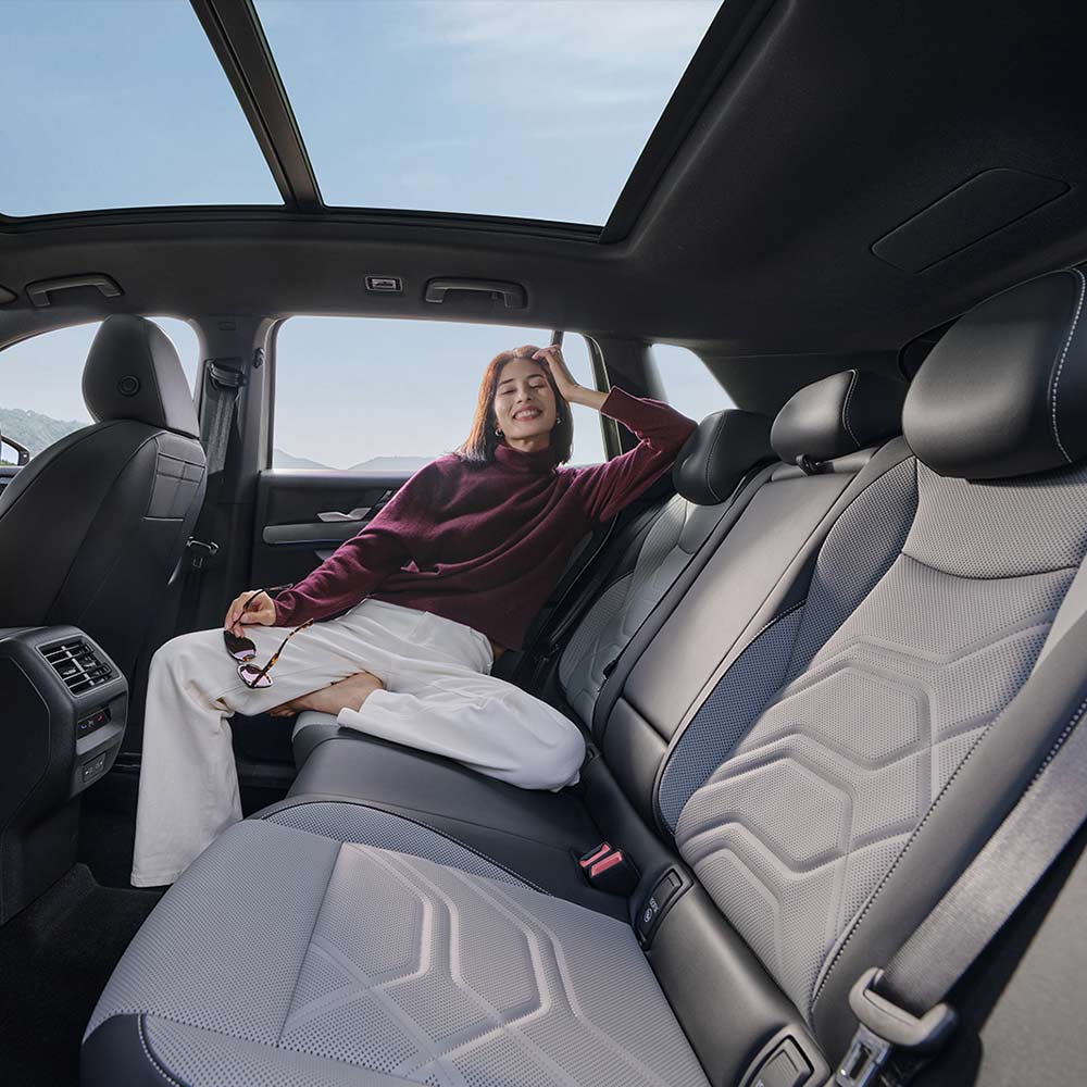 VW-All-New-Tayron-L-2025-300TSI-2WD-Elite-Interior-Rear-Space A woman relaxing in the spacious back seat of a car with a panoramic sunroof.