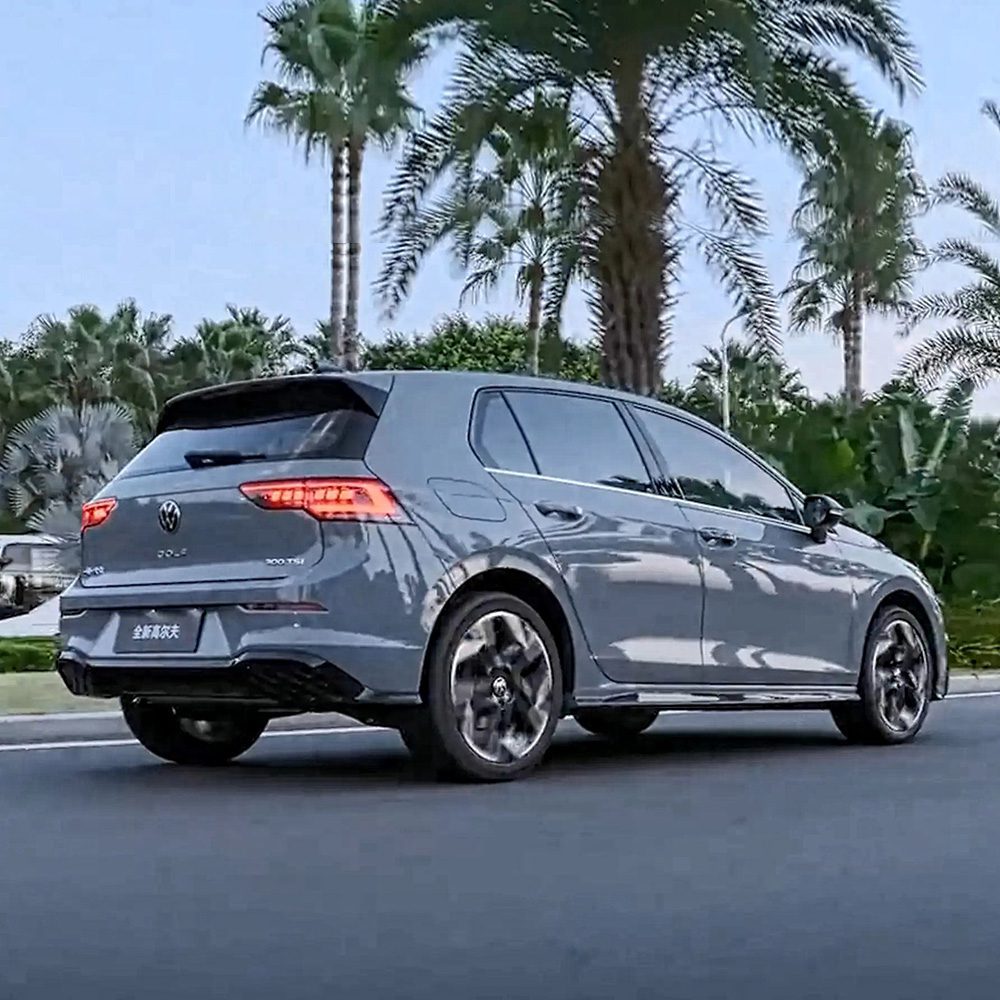 A gray Volkswagen Golf driving on a road with palm trees in the background.
