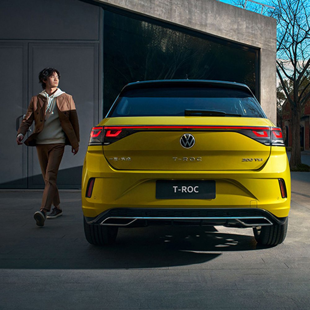 Rear view of a yellow Volkswagen T-ROC with a person walking beside it.
