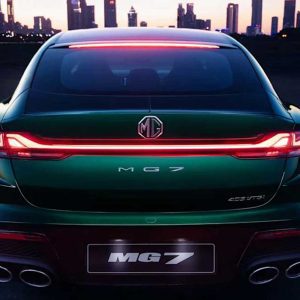 The rear view of a green MG7 car with illuminated taillights, set against a city skyline at dusk.