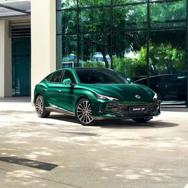 Two MG cars, one green and one silver, parked in front of a modern glass building under a clear blue sky.
