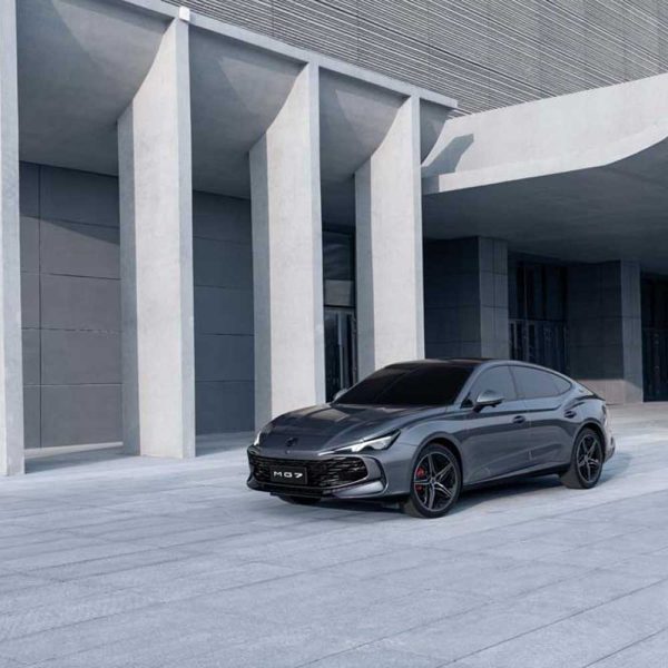 A gray MG7 car parked in front of a modern building with large concrete pillars.