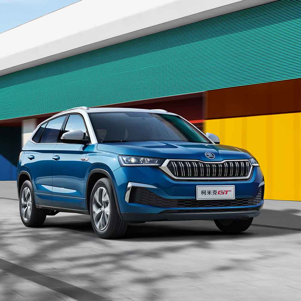 SKODA KAMIQ GT 2025 1.5L Automatic Premium Edition Hero Shot Blue Skoda Kamiq GT SUV driving past a colorful building.
