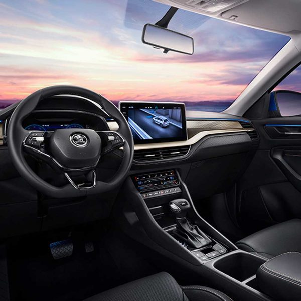 Interior of a Skoda car showing the steering wheel, infotainment screen with navigation, and dashboard, with a sunset sky visible through the windshield.