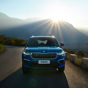 SKODA KODIAQ 2025 TSI330 5-Seater FWD Luxury Edition gallery image Front Elevation A blue Skoda Kodiaq SUV on a winding mountain road with the sun shining behind the mountains.