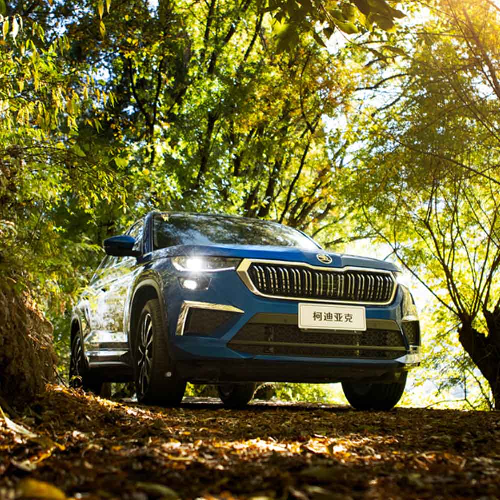 SKODA KODIAQ 2025 TSI330 5-Seater FWD Luxury Edition gallery image Real Shot 2 A blue Skoda Kodiaq SUV driving on a forest path with sunlight filtering through the trees.