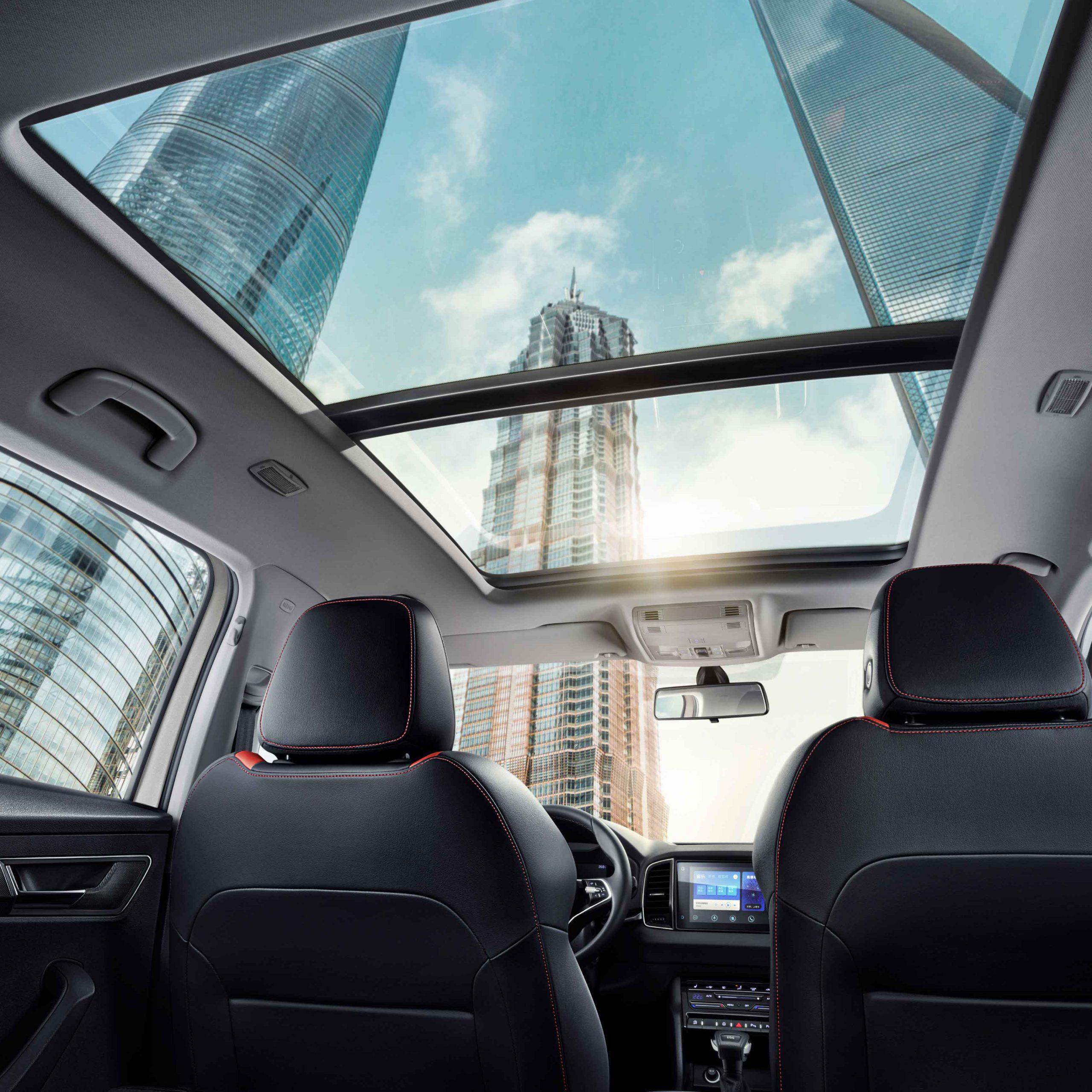Interior of a car with a panoramic sunroof, showing tall city buildings outside.