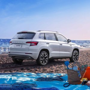 A white Skoda Karoq SUV parked on a sandy beach, with the sea and beach items in the foreground.