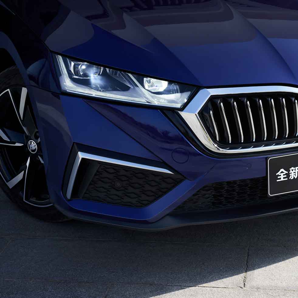 Close - up of the front of a blue Skoda car, showcasing its headlight and grille.