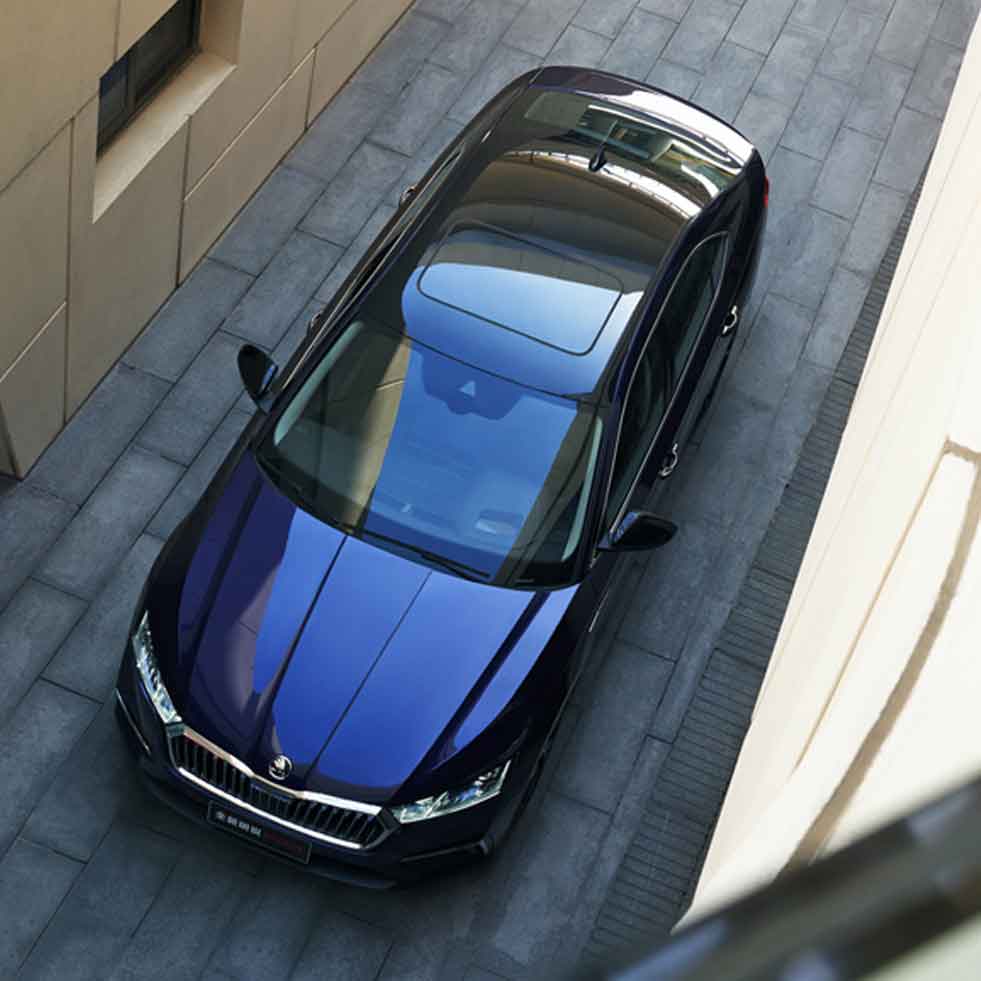 A Skoda car, with its sleek design and shiny blue exterior, parked in an urban setting between buildings.