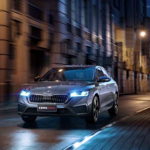 A silver Skoda Octavia Pro car driving on a city street at night, with buildings and lights in the background.