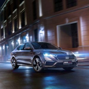 A silver Skoda Octavia Pro car driving on a city street at night, with buildings and lights in the background.