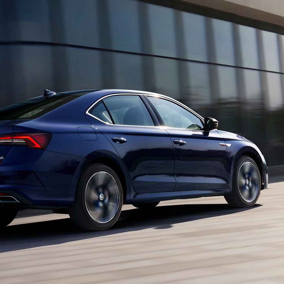 A blue sedan in motion, with a modern building in the background.