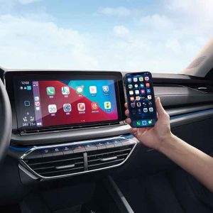 A hand holding a smartphone, mirroring apps on the car's infotainment screen, with a blue sky in the background.