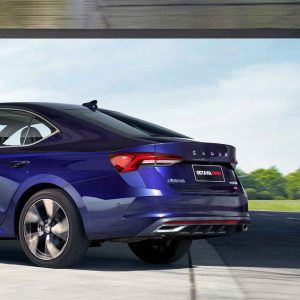 Rear view of a blue Skoda Octavia Pro car in motion, with a clear sky and greenery in the background.