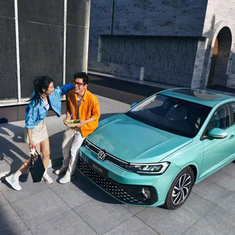 A man and a woman interacting beside a turquoise Volkswagen Lavida XR sedan.