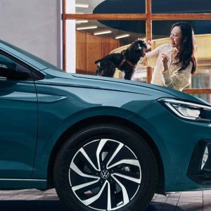 A woman interacting with a dog near a teal Volkswagen car.