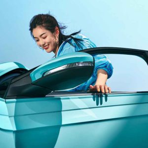 A woman leaning out of a turquoise car window under a clear blue sky.
