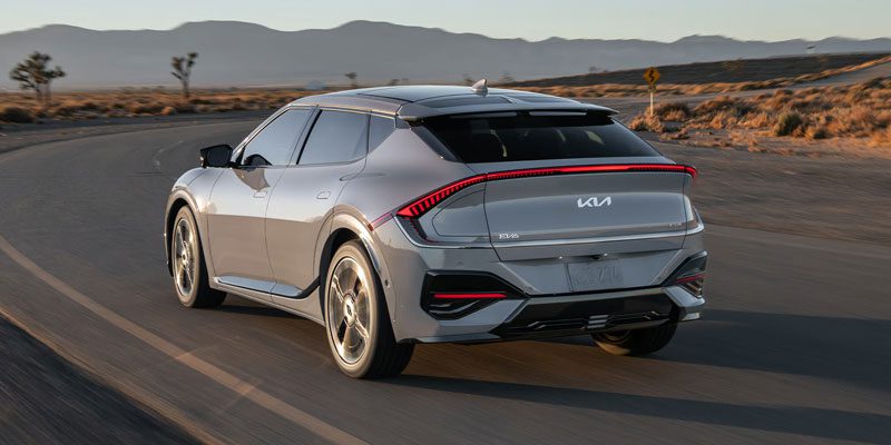 2025 Kia EV6, three quarter back view, driving on a curved road in the desert showcasing stylish headlights and a redesigned silhouette