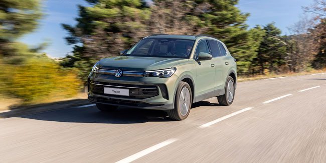 A green Volkswagen Tiguan driving down a road with lush greenery beside it
