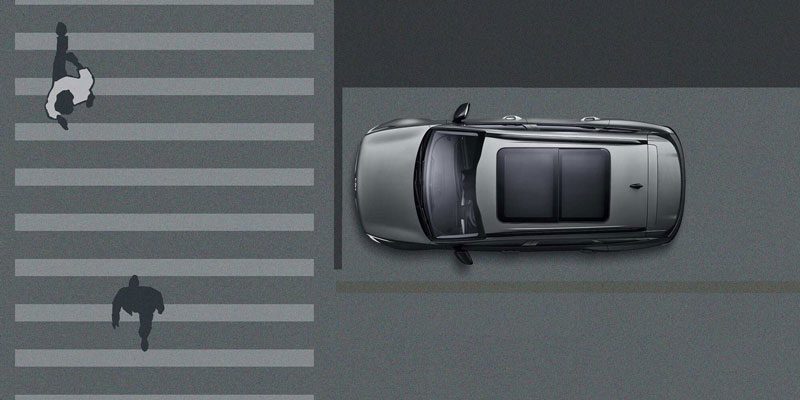 Top-down diagram: a dark car adjacent to a crosswalk where two figures (one falling, one running) are depicted. Likely illustrates a pedestrian safety feature (e.g., automatic emergency braking) in a vehicle.