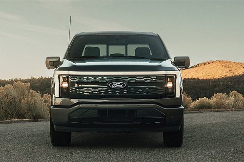 A 2025 Ford F-150 Lightning in Carbonized Gray parked with a hilly terrain in the background