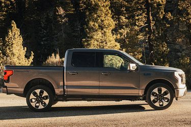 A 2025 Ford F-150 Lightning in Iconic Silver parked on a paved road showing off the side profile