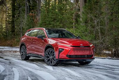 Vibrant red Toyota SUV driving on a snow-dusted forest road, surrounded by tall evergreen trees.