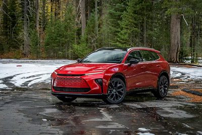 Vibrant red Toyota SUV parked on a wet, snow-dusted forest road, surrounded by evergreen trees.