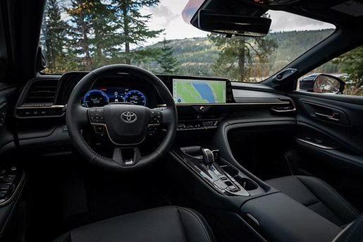 Black interior of a Toyota vehicle, showcasing the digital dashboard, infotainment screen, and steering wheel with a scenic view outside.