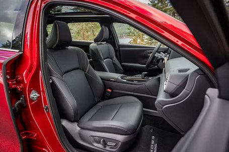 Black leather front passenger interior of a red SUV, with a panoramic view of trees visible through the open door.