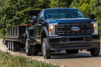 2026 Ford Super Duty pickup pulling a large flat bed trailer up a paved hill