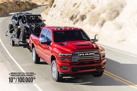 A red 2026 Ram 2500 Laramie 4x4 Crew Cab traveling on a highway in the mountains, while towing two ATVs.