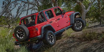 Display A red 2025 Jeep Wrangler Rubicon 4xe ascending a steep hill off-road
